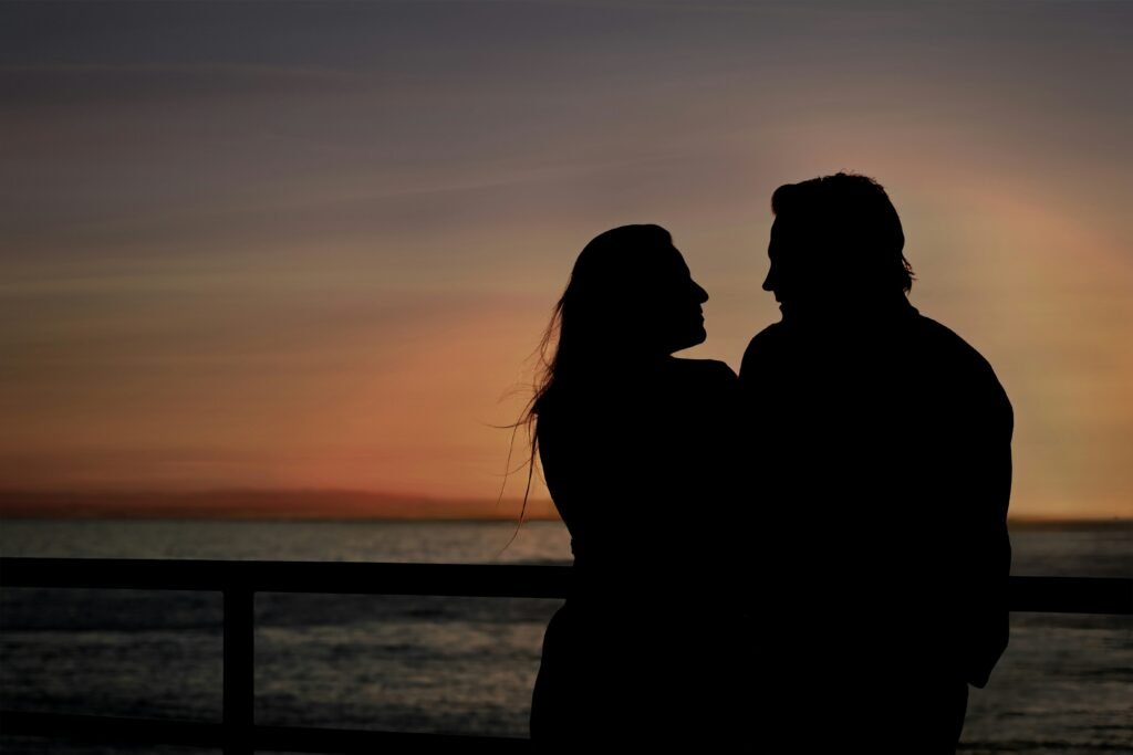 Couple embraces at sunset, silhouetted by sky.